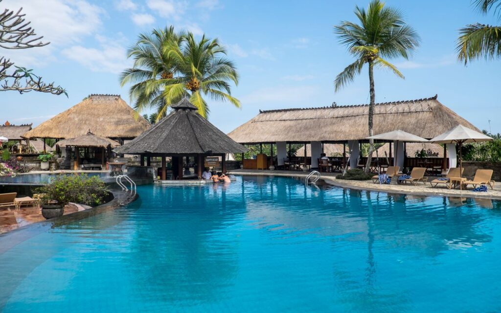 Relax by the tropical pool at a luxurious resort in Bali, featuring palm trees and serene blue waters.